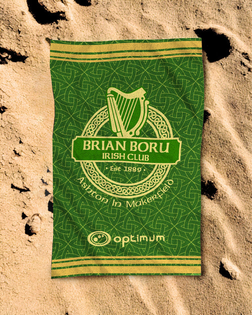 Green and yellow beach towel of Brian Boru Irish Club on a sandy background